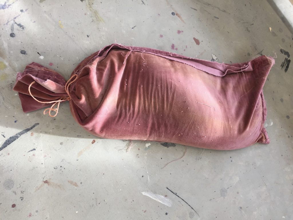 Pink velvet sack filled with something on paint-splattered floor.